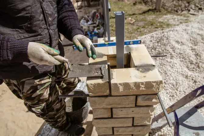 Worker laying bricks around a metal post at an outdoor construction site