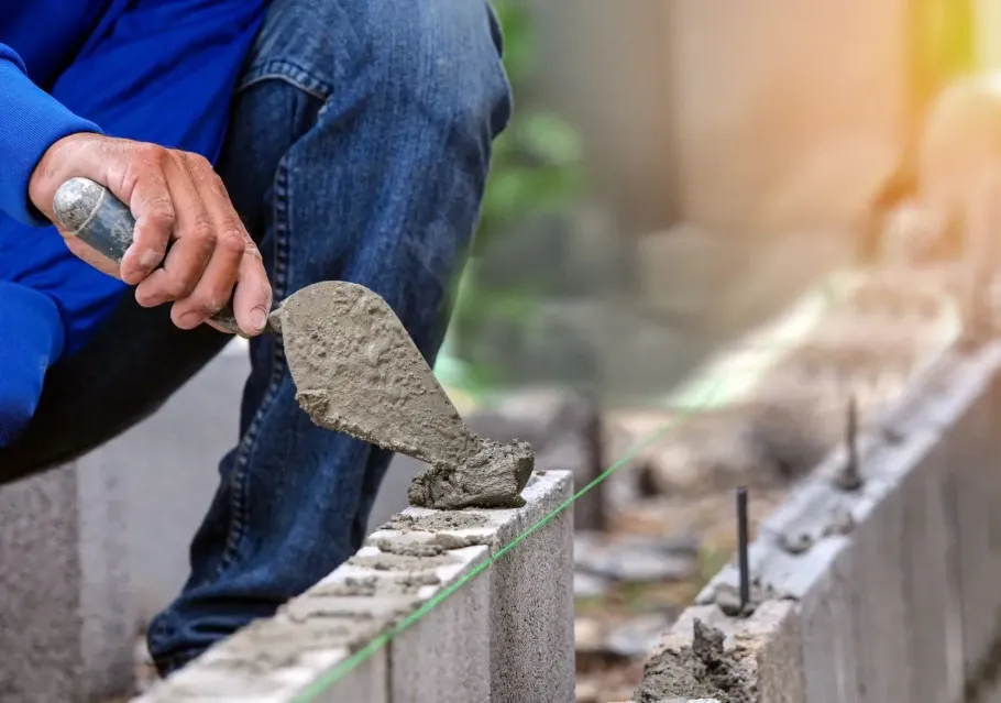Worker spreading wet concrete with a trowel along a curb outdoors