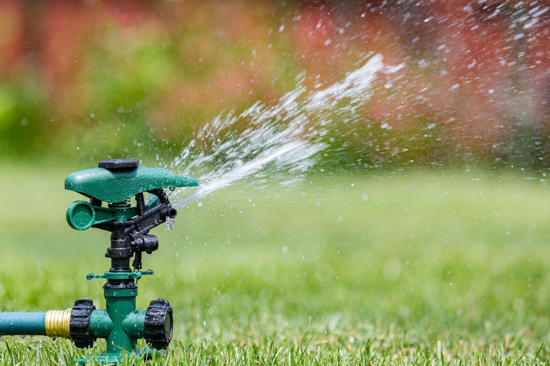 Green lawn sprinkler spraying water onto a grassy lawn.
