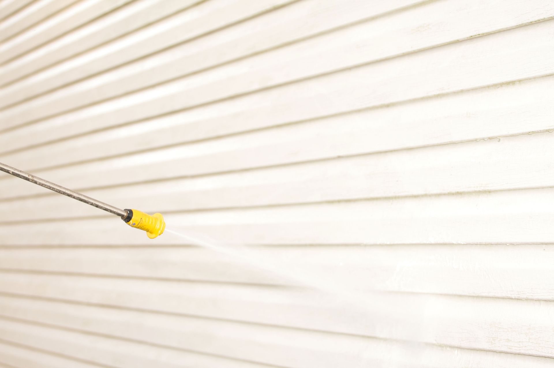 A pressure washer spraying water onto white siding.