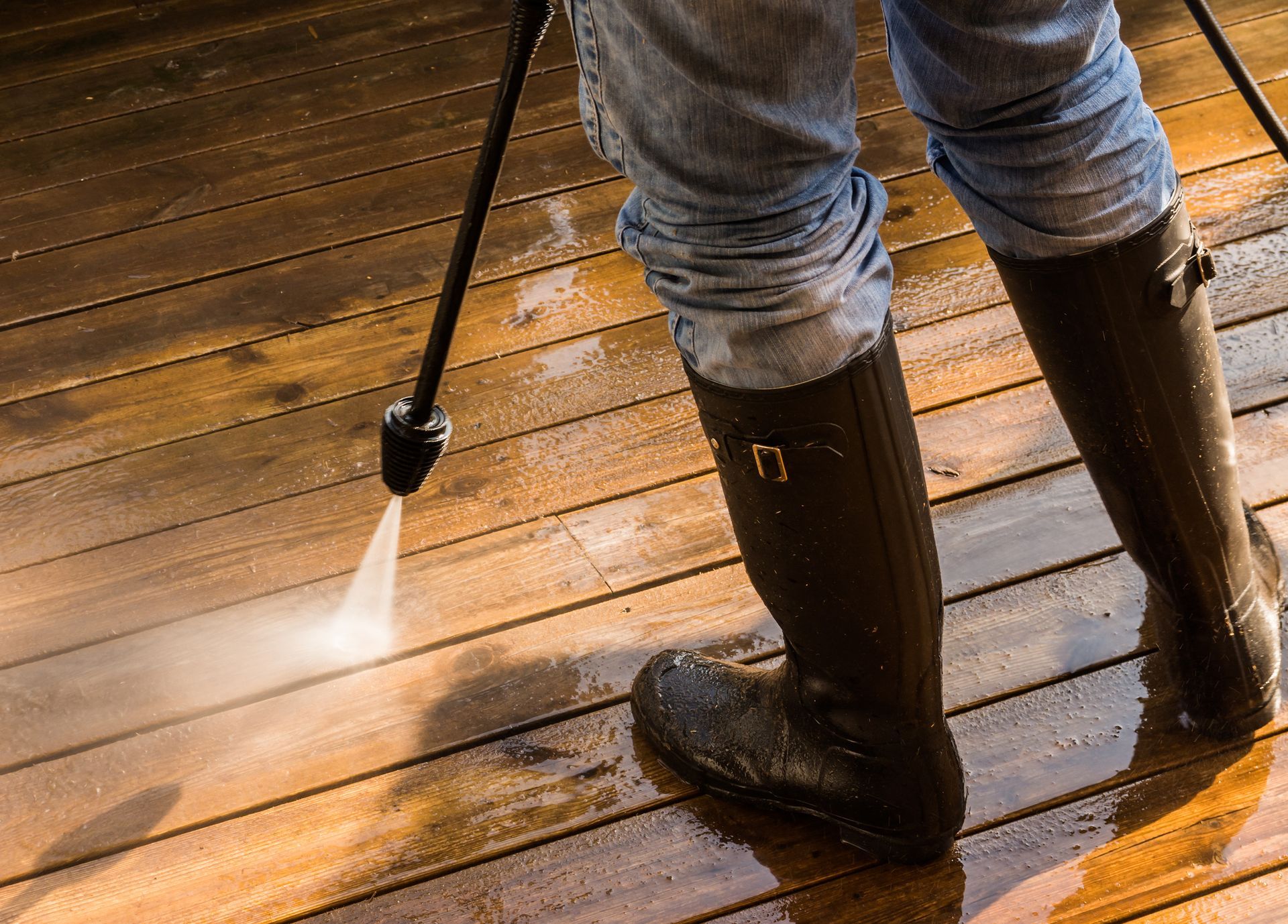 Person in rubber boots power washing a wooden deck.