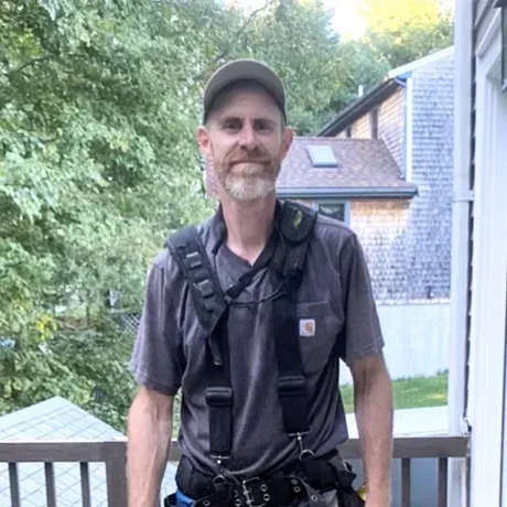 A man wearing a harness and a hat is standing on a balcony.