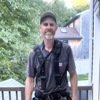 A man wearing a harness and a hat is standing on a balcony.