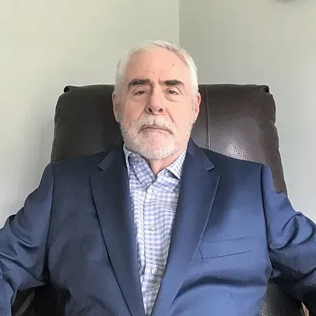 A man in a suit and plaid shirt is sitting in a chair.