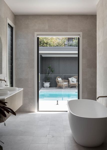 Bathroom with open doorway to pool. White tub, beige walls, wood vanity, pool with seating.