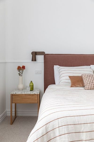 Bedroom with a bed, nightstand, vase with flowers, and wall-mounted light. Soft tones and neutral colors.