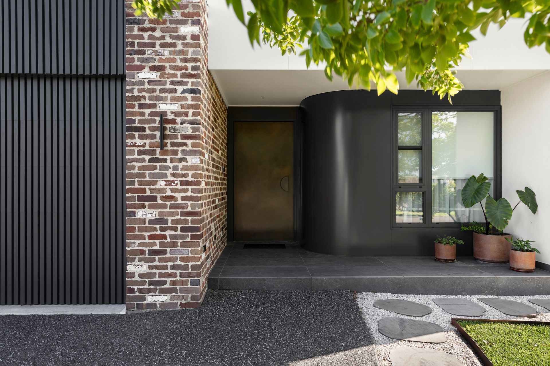 Modern house entryway with brick wall, dark siding, potted plants, and a covered front porch