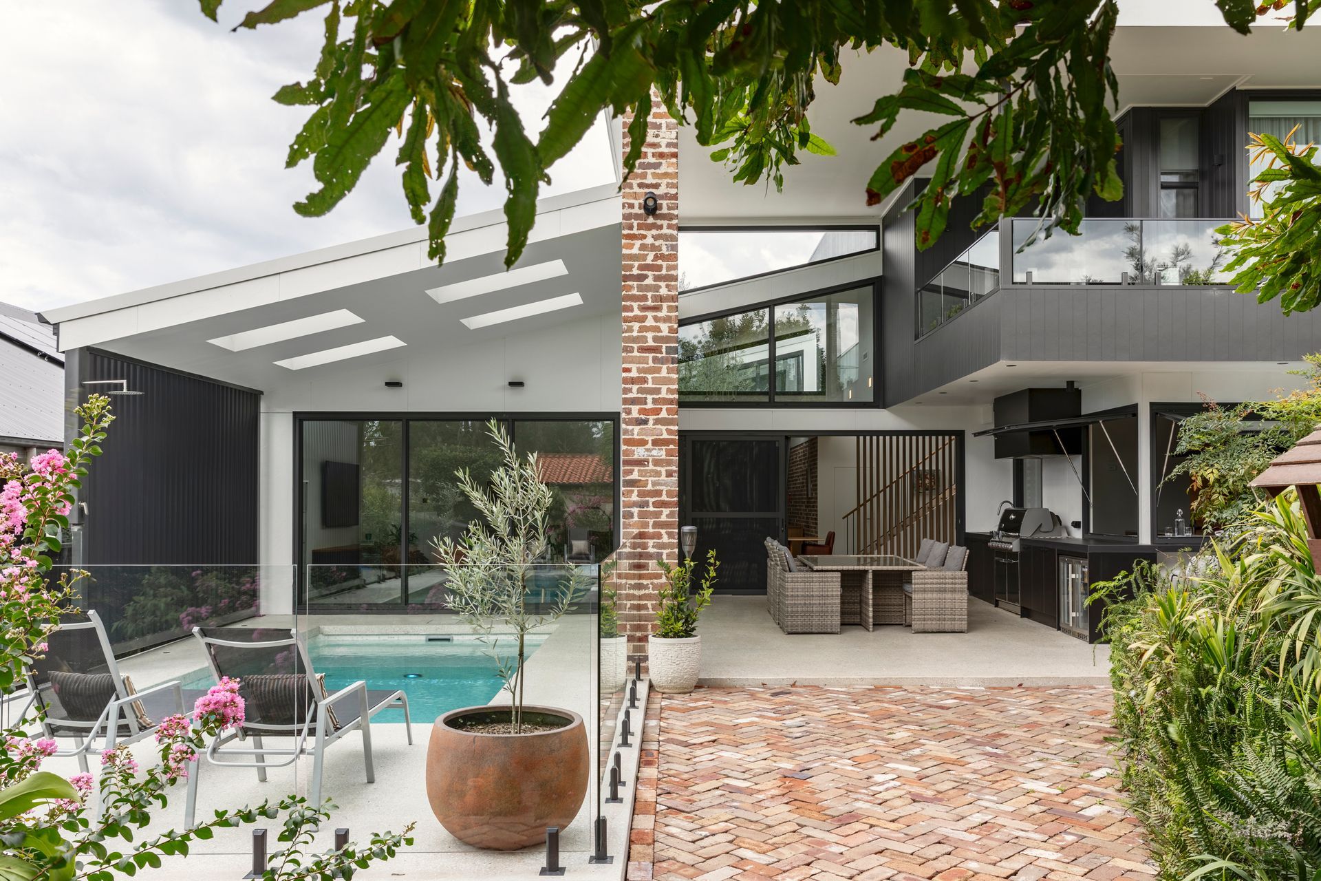 Modern house patio with pool, brick column, outdoor seating, and lush greenery under a covered terrace