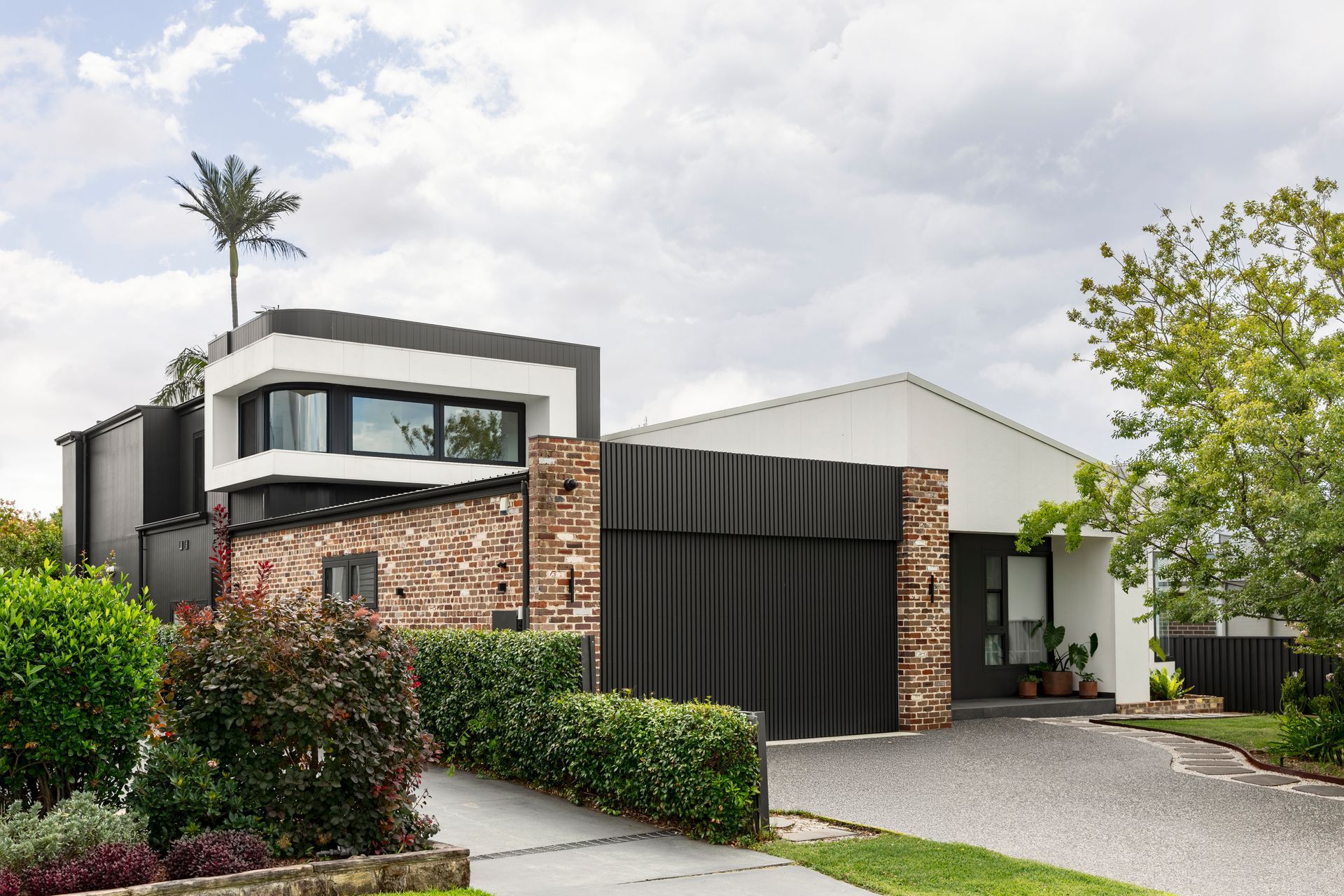 Modern two-story house with stone and black facade, driveway, and landscaped front yard
