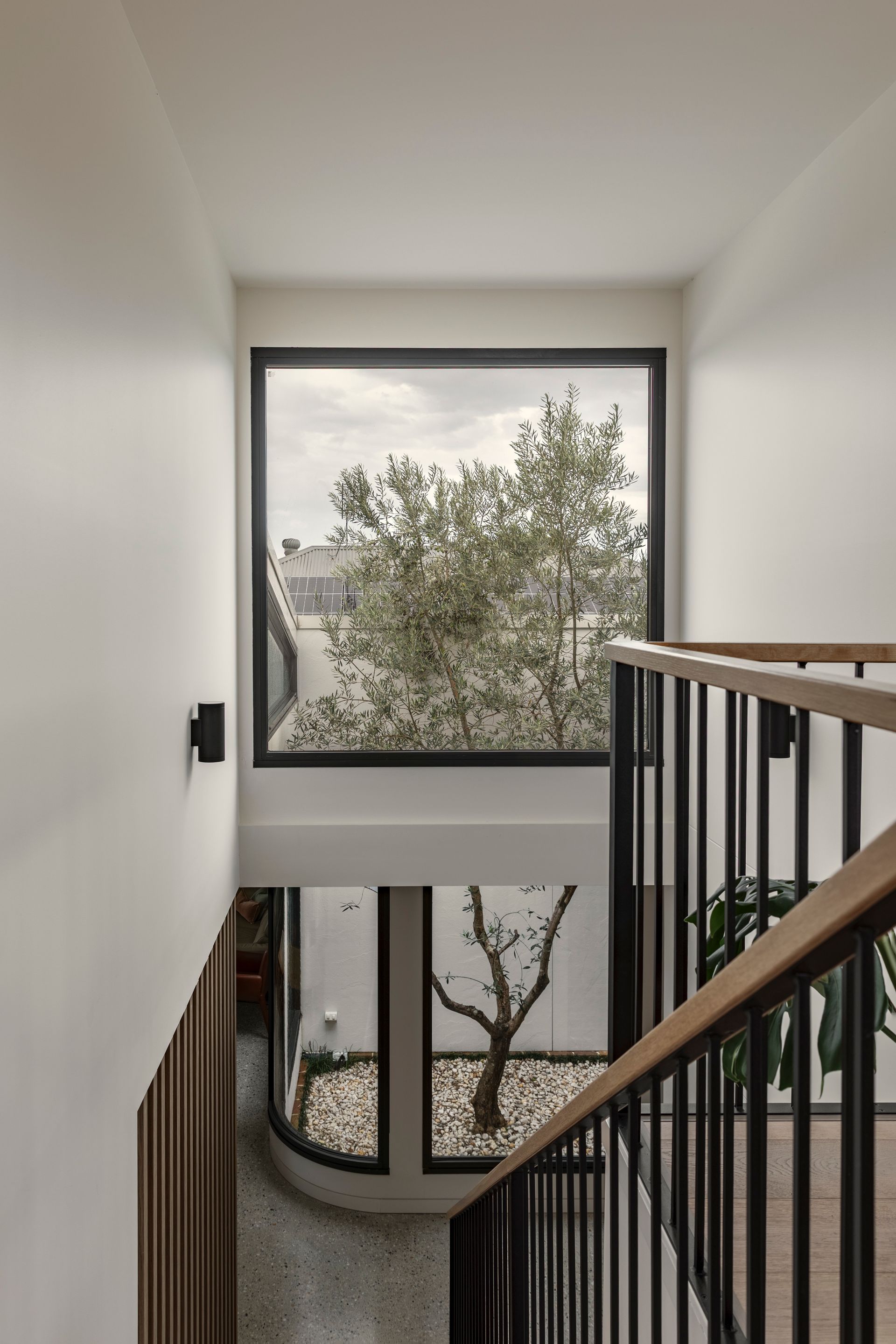 Modern stairwell with white walls, black railings, and a large window overlooking trees.
