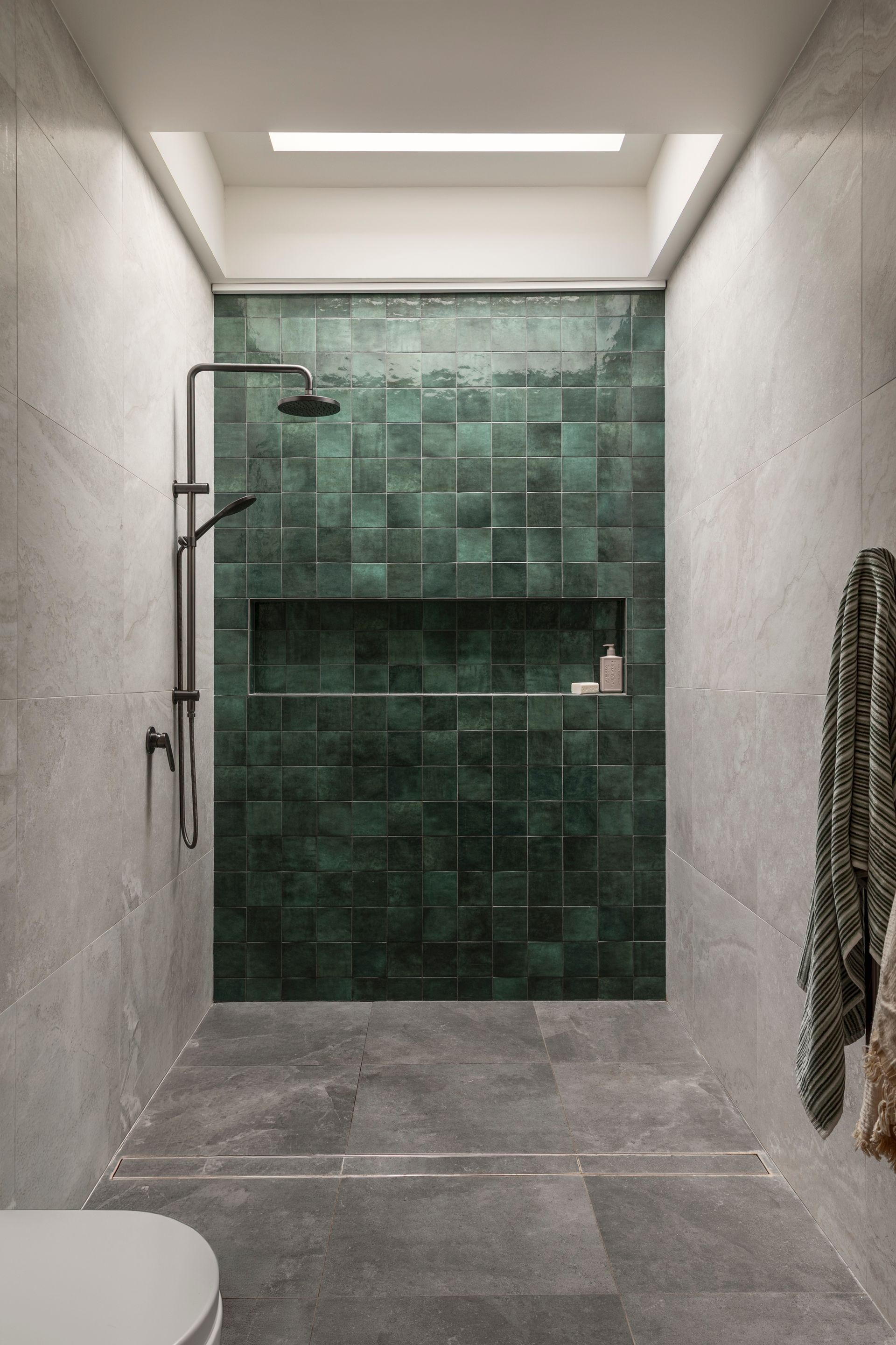 Narrow tiled shower with green accent wall, gray floor, and hanging towels.