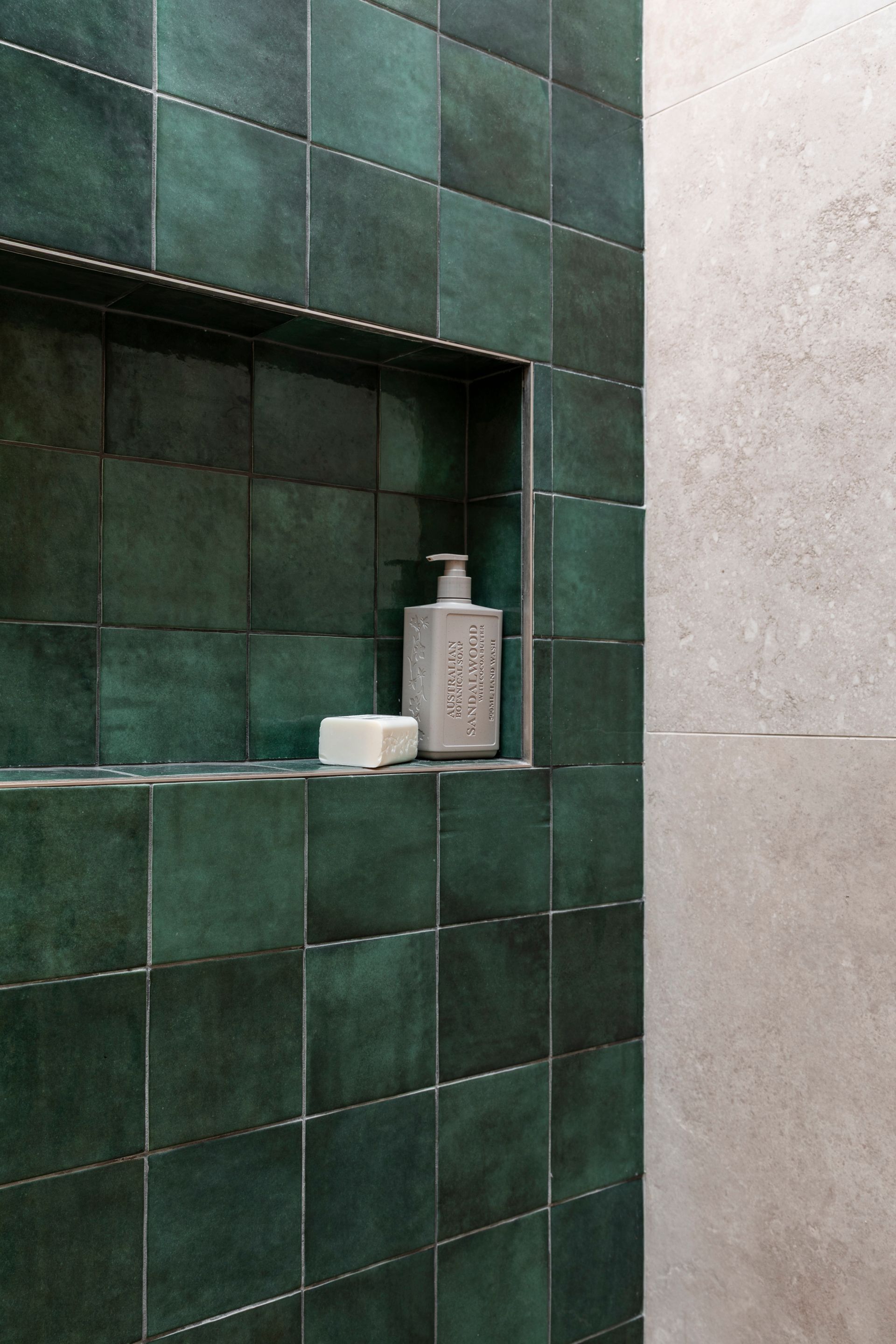 Green tiled shower niche with a soap dispenser and bar of soap on a shelf