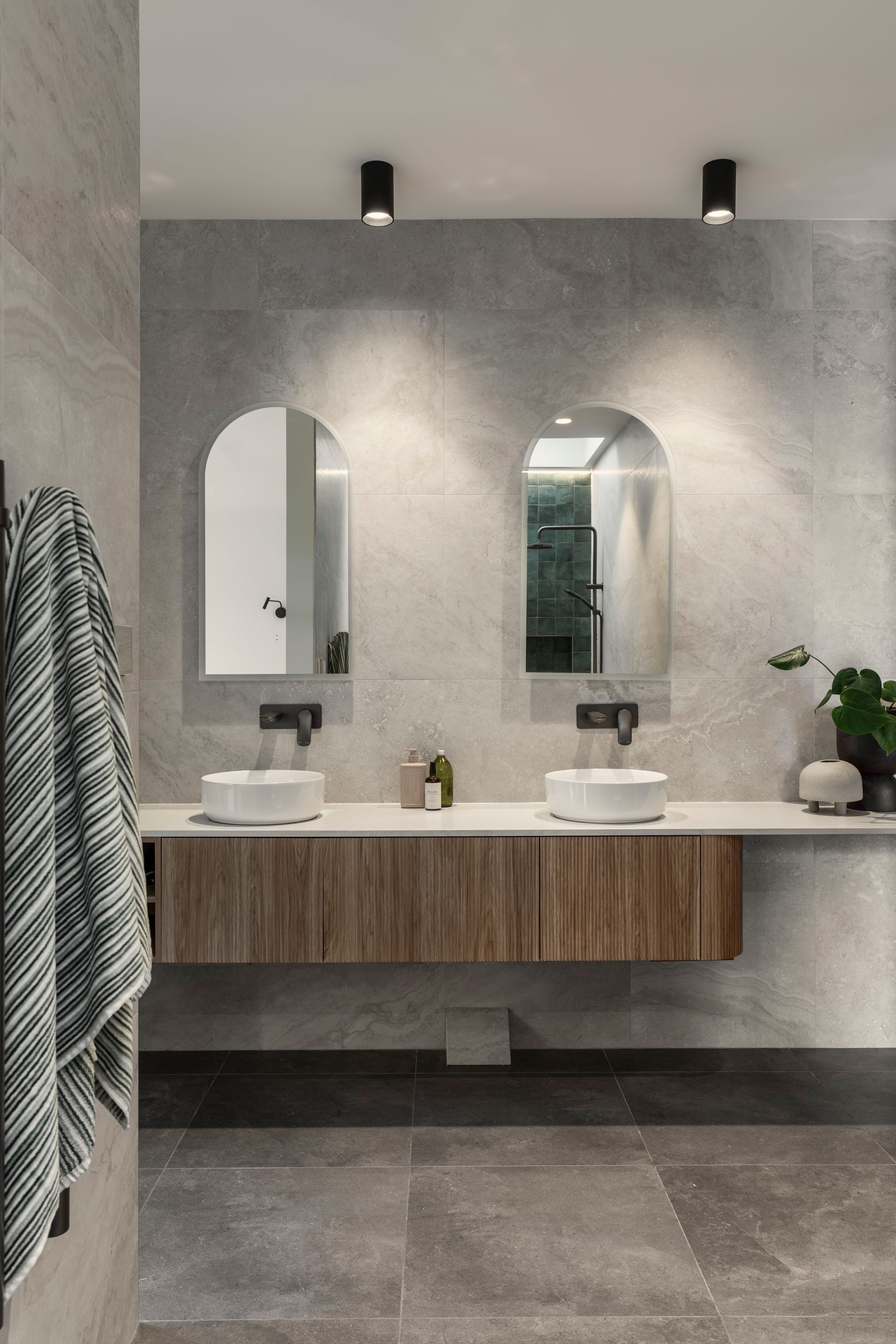 Modern bathroom with double sinks, arched mirrors, and gray stone walls and floor