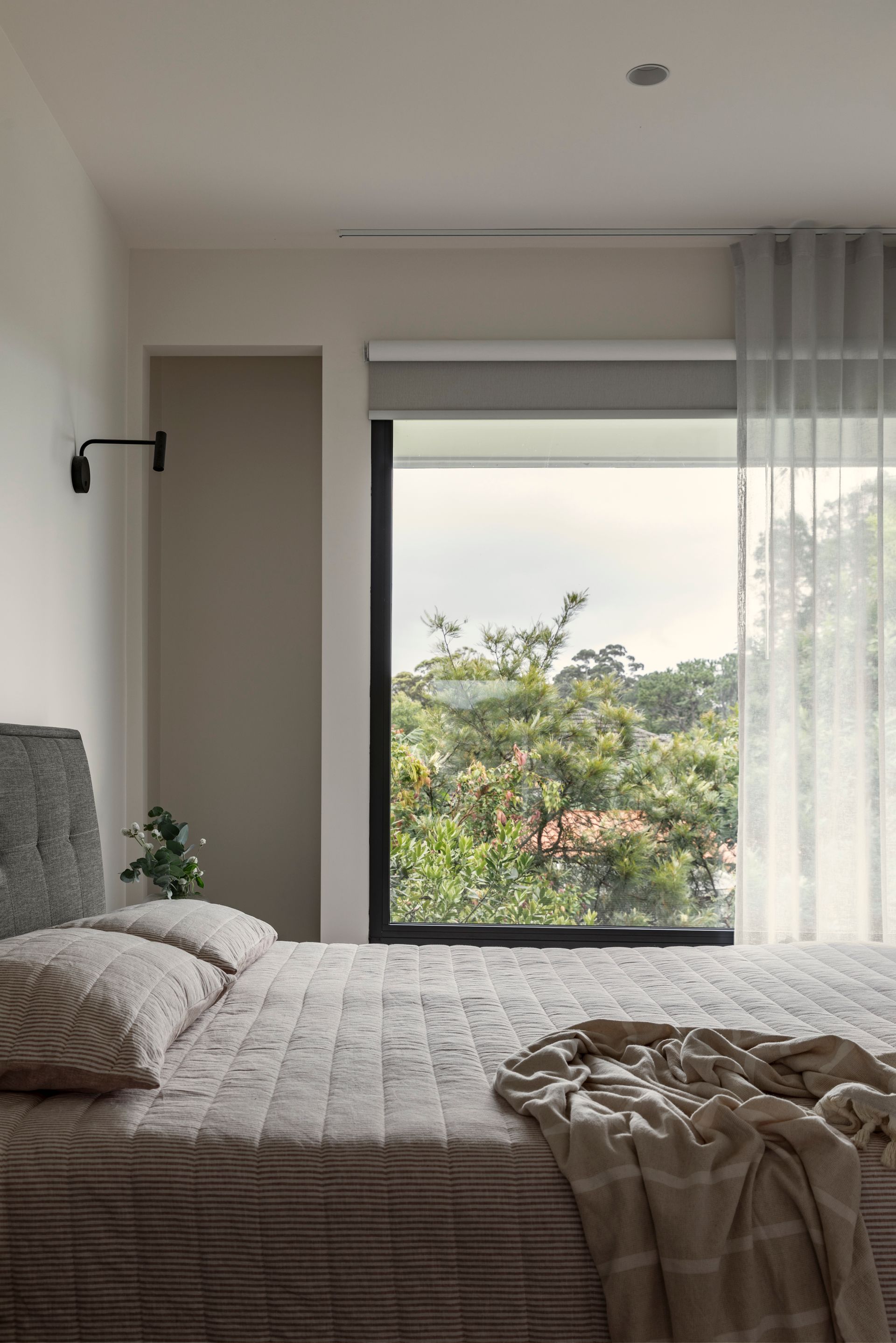 Cozy bedroom with an unmade bed, window seat, and view of green trees outside.