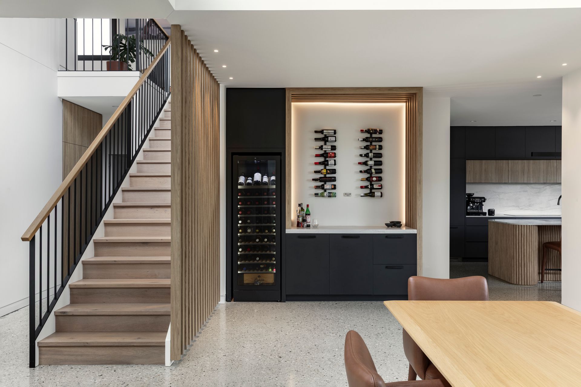Modern open-plan home interior with staircase, wine fridge, built-in shelves, and kitchen island