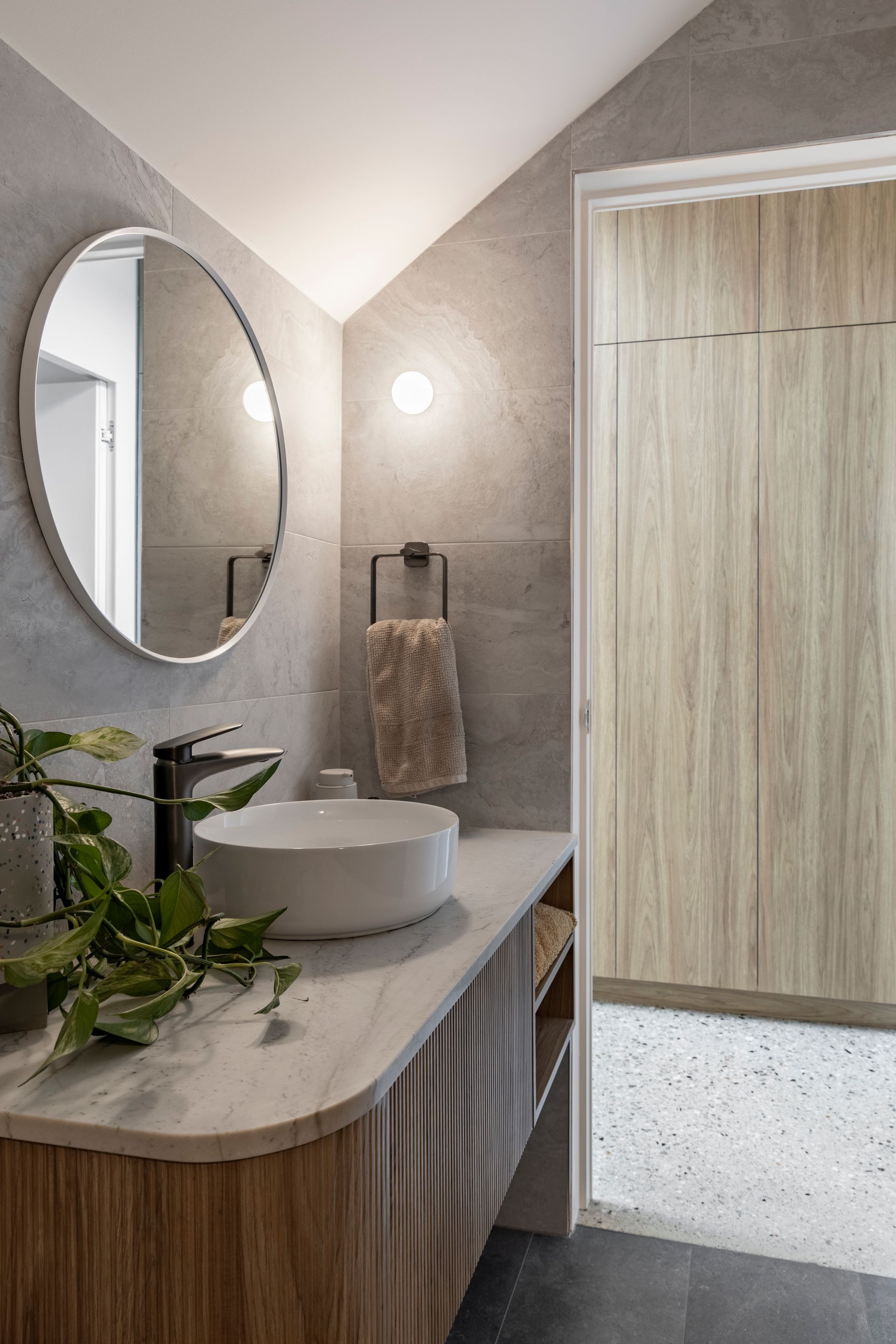 Modern bathroom vanity with oval mirror, round sink, wood cabinetry, towel, and sliding wood door.