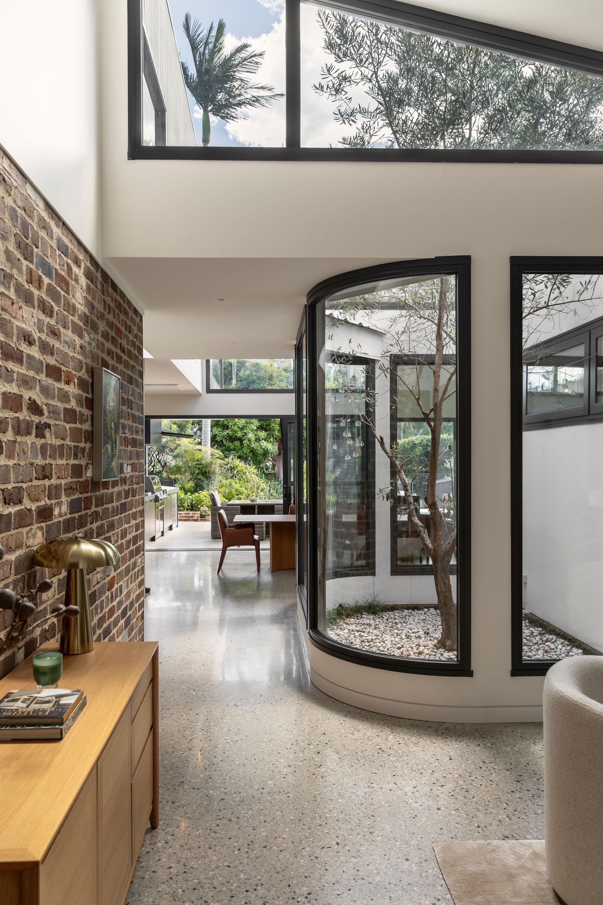 Modern interior with brick wall, curved glass doorway, terrazzo floor, and greenery outside。