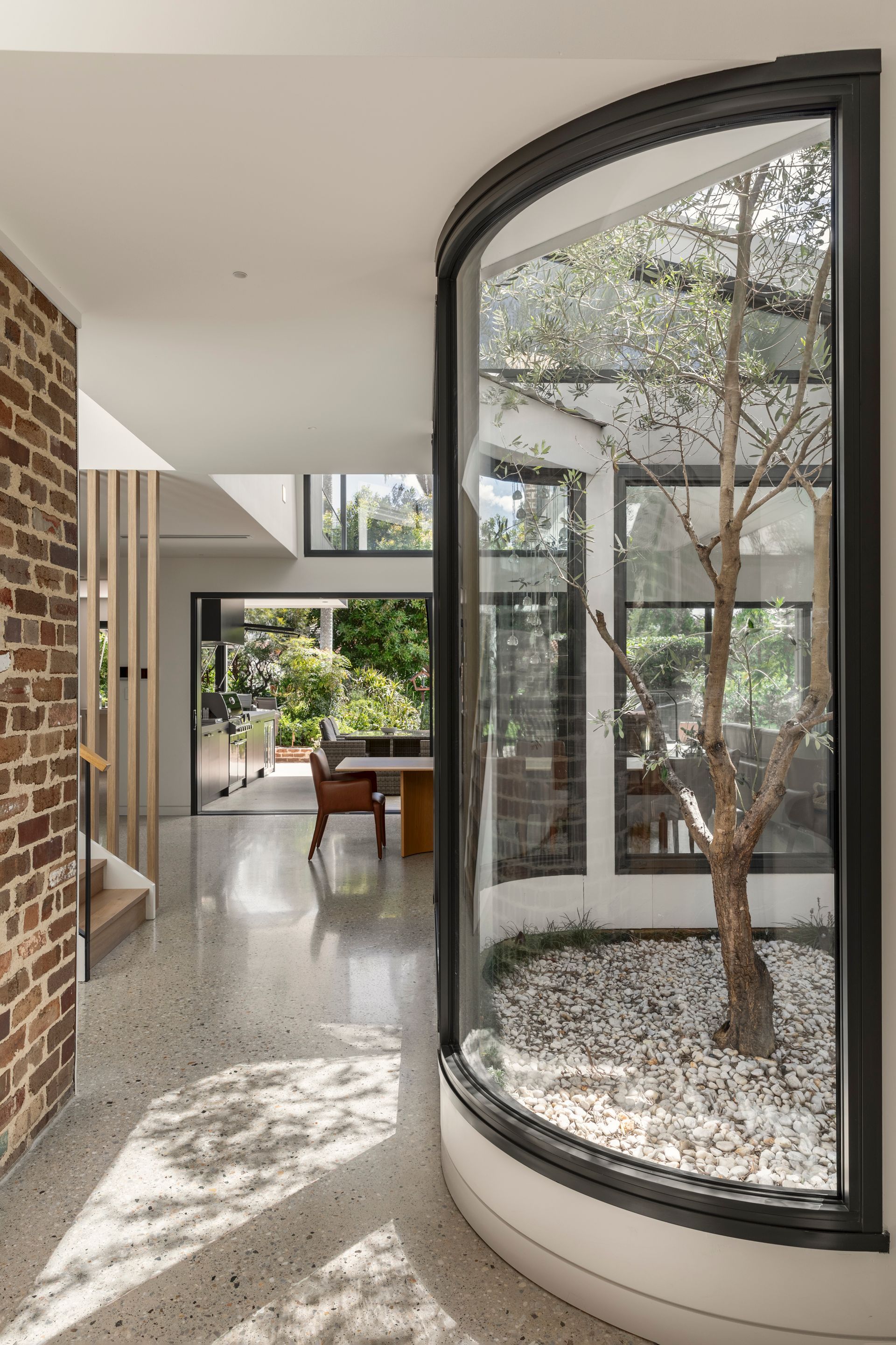 Modern hallway with curved glass planter, brick wall, polished floor, and a pool table at the far end