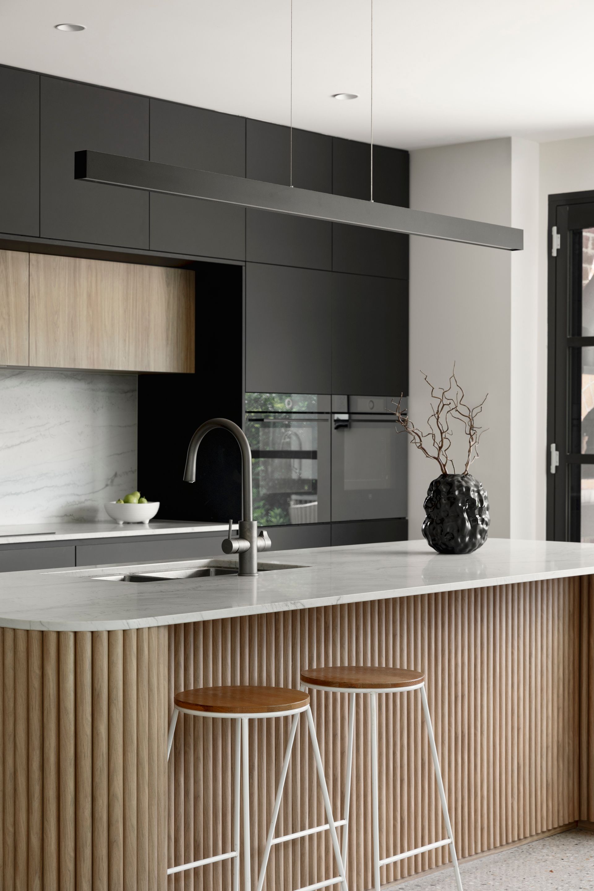Modern kitchen with black cabinets, wood island, marble countertop, and two stools