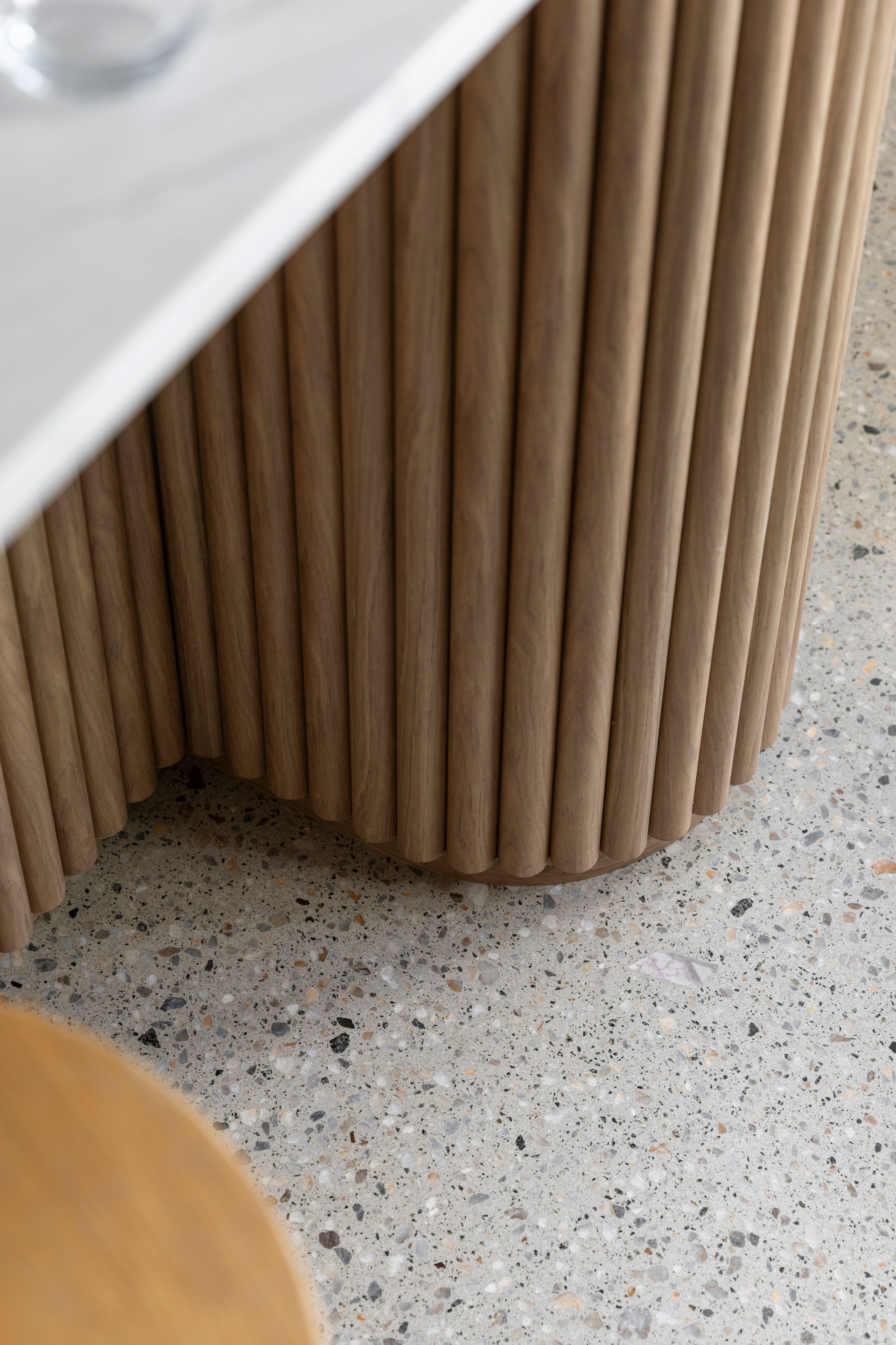 Close-up of a round, ribbed wooden table base on a speckled floor under a white tabletop