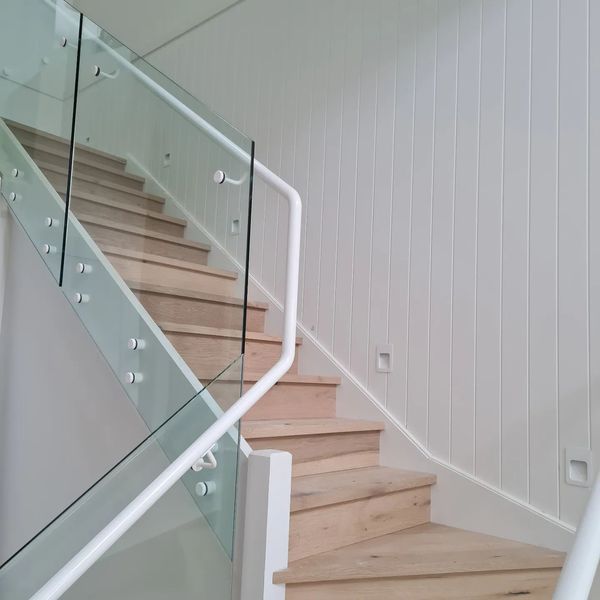 Staircase with wooden steps and glass panel railing, white walls and handrail.