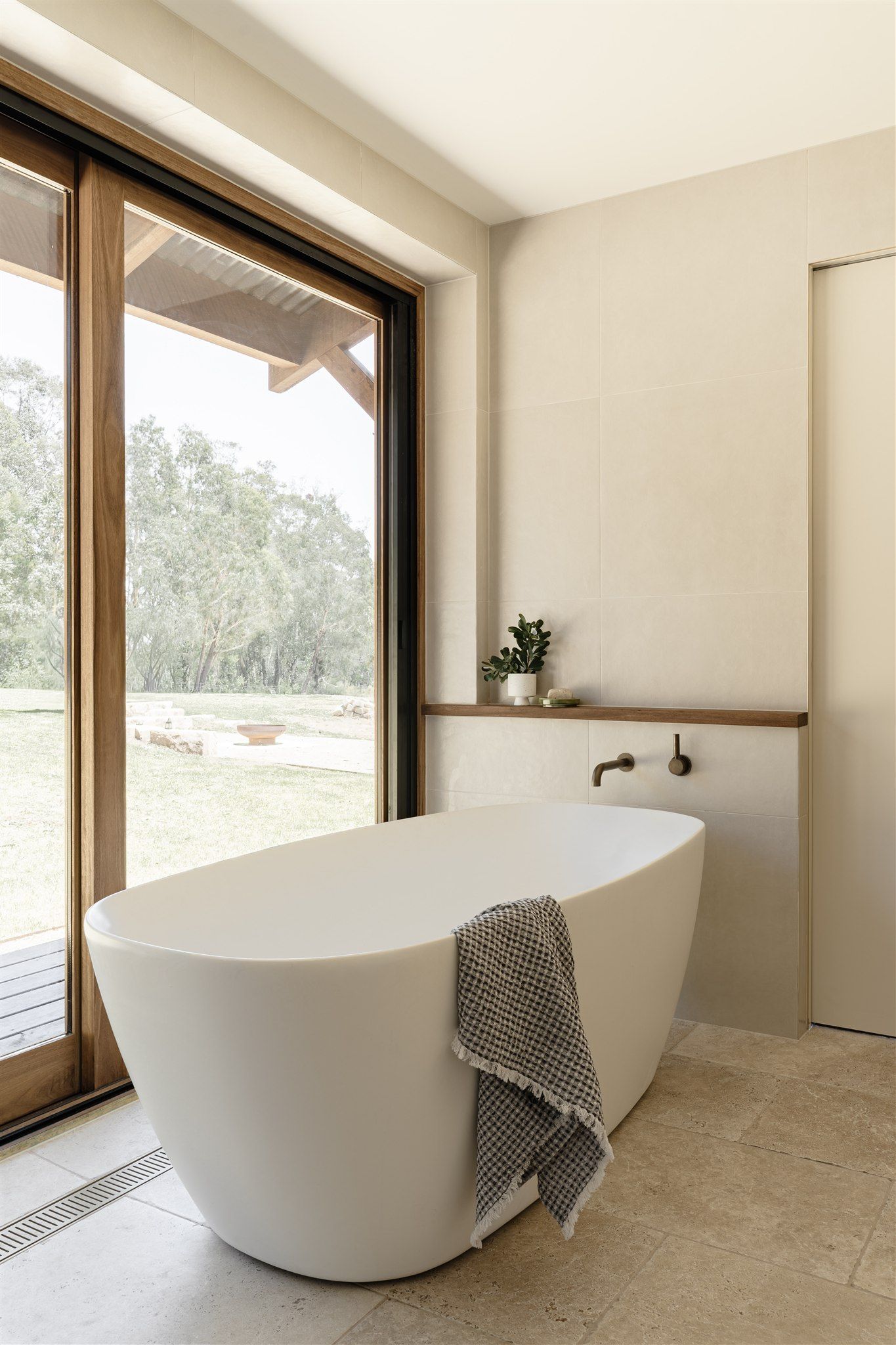 A modern, minimalist bathroom features a white freestanding bathtub next to a large floor-to-ceiling window.