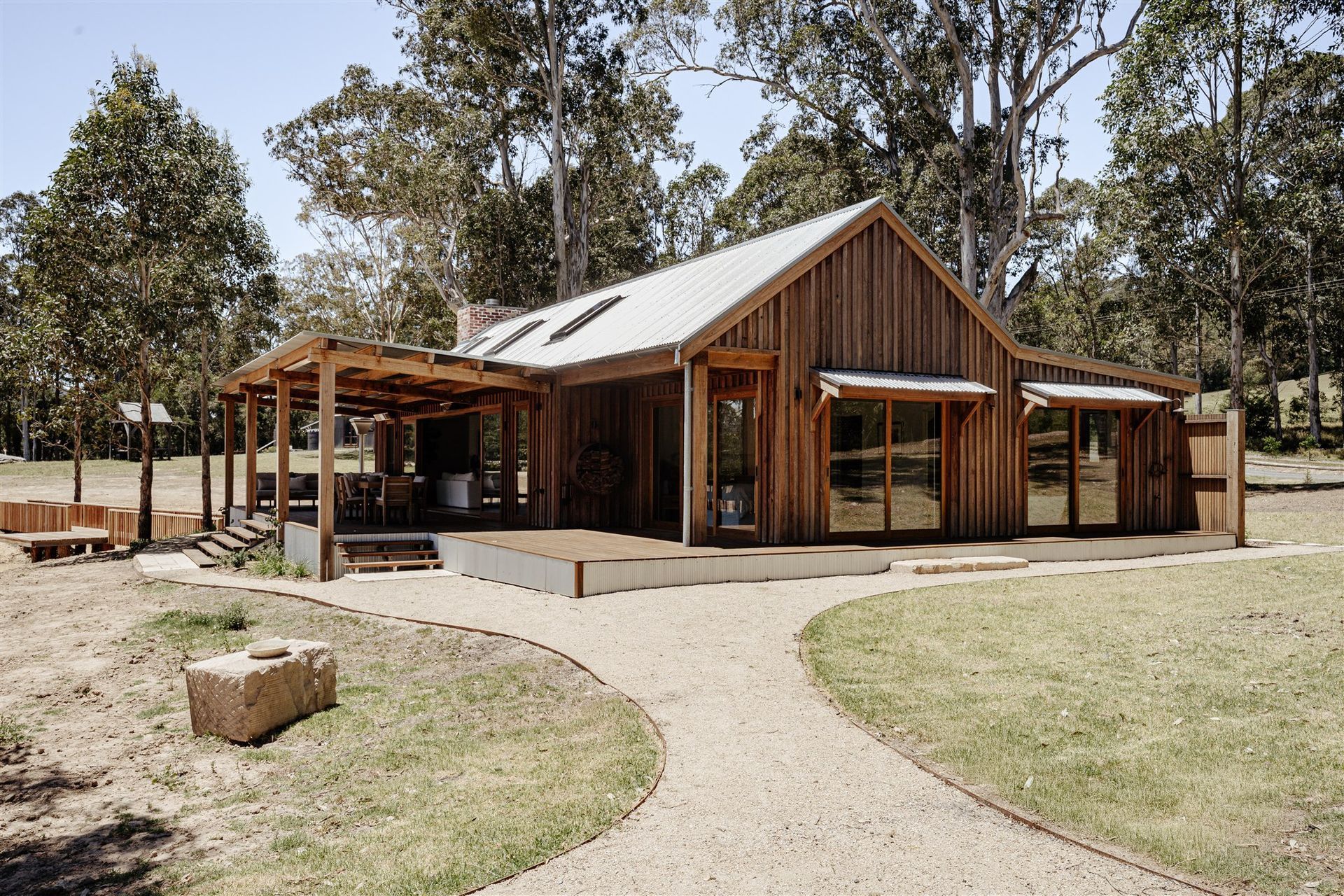 A modern rustic cabin made of vertical wood planks with a metal roof, set in a natural, wooded landscape.