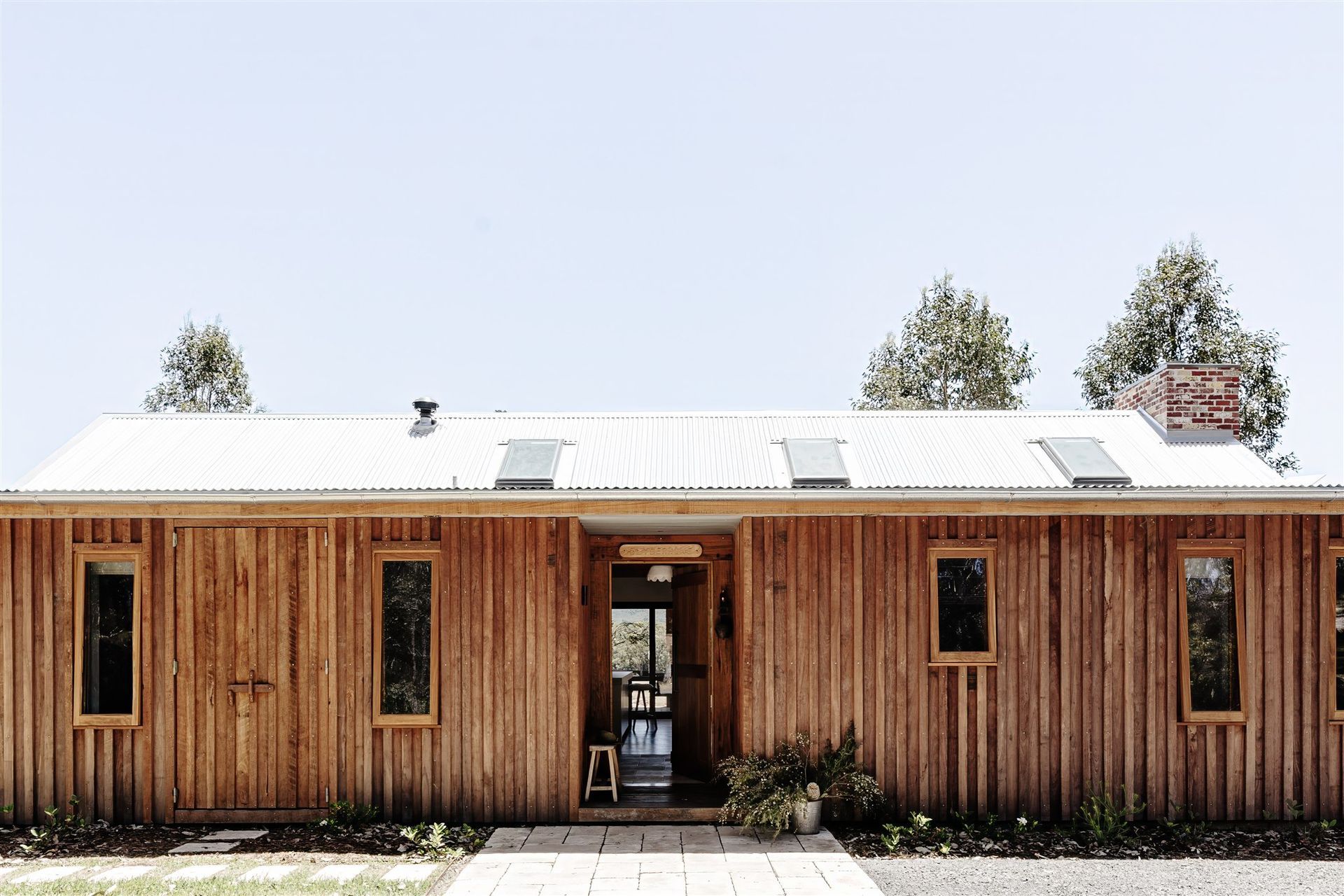 A single-story rustic cabin with vertical wood siding, a metal roof, and rectangular windows under a clear blue sky.
