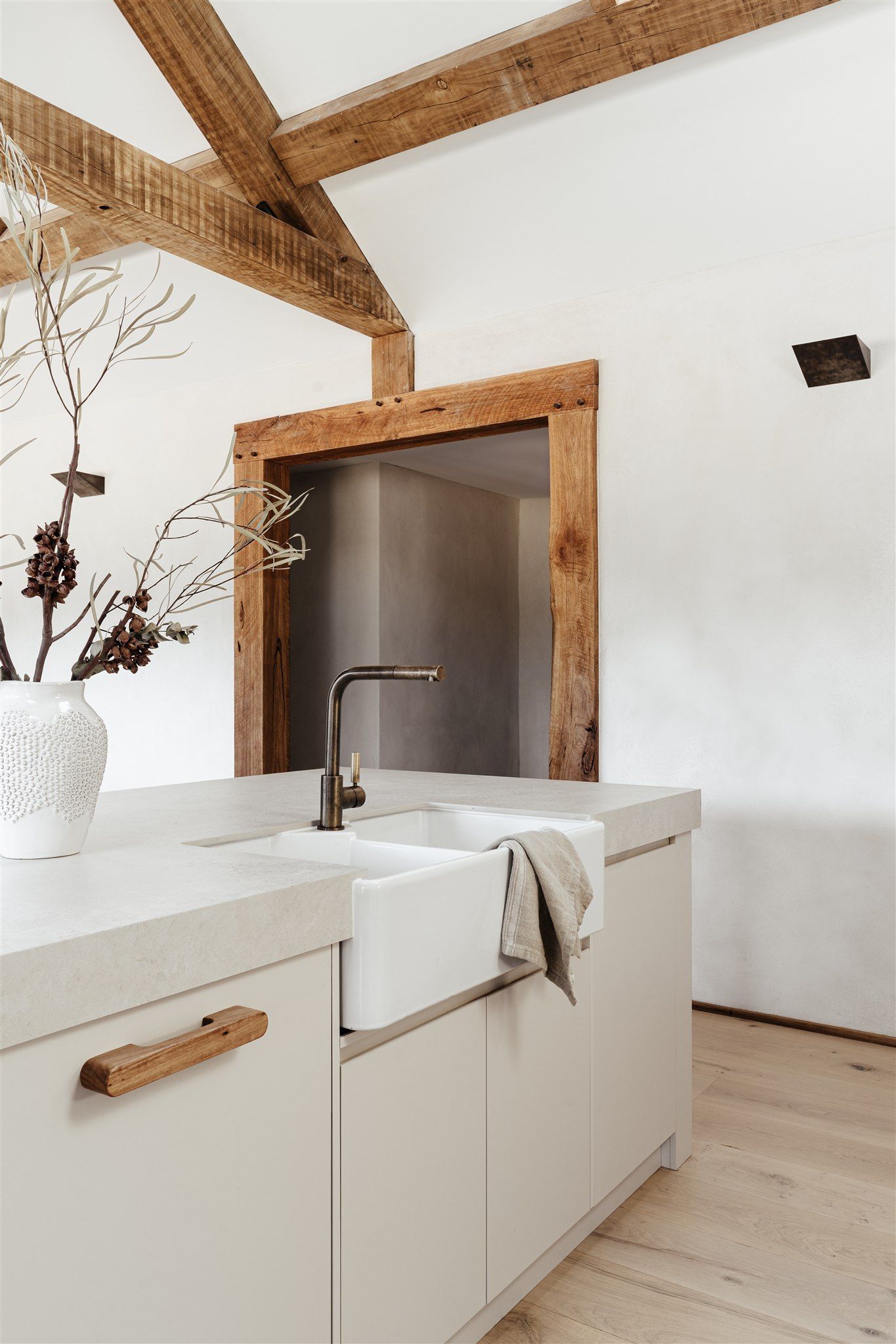 A kitchen island with a farmhouse sink and wooden handle, set against white walls and exposed timber ceiling beams.