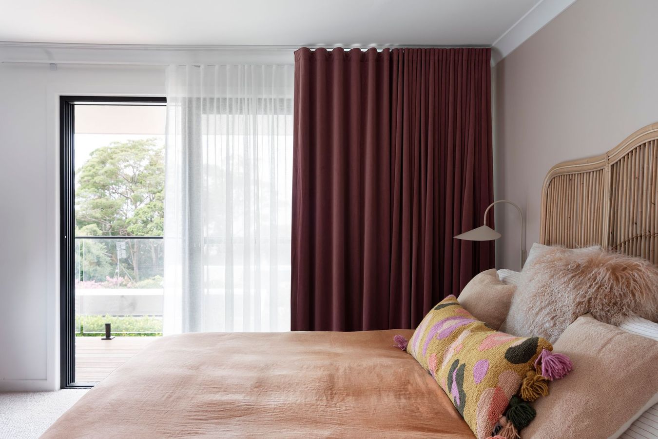 Bedroom with a bed, window, and burgundy curtains. A pink blanket and pillows decorate the bed.