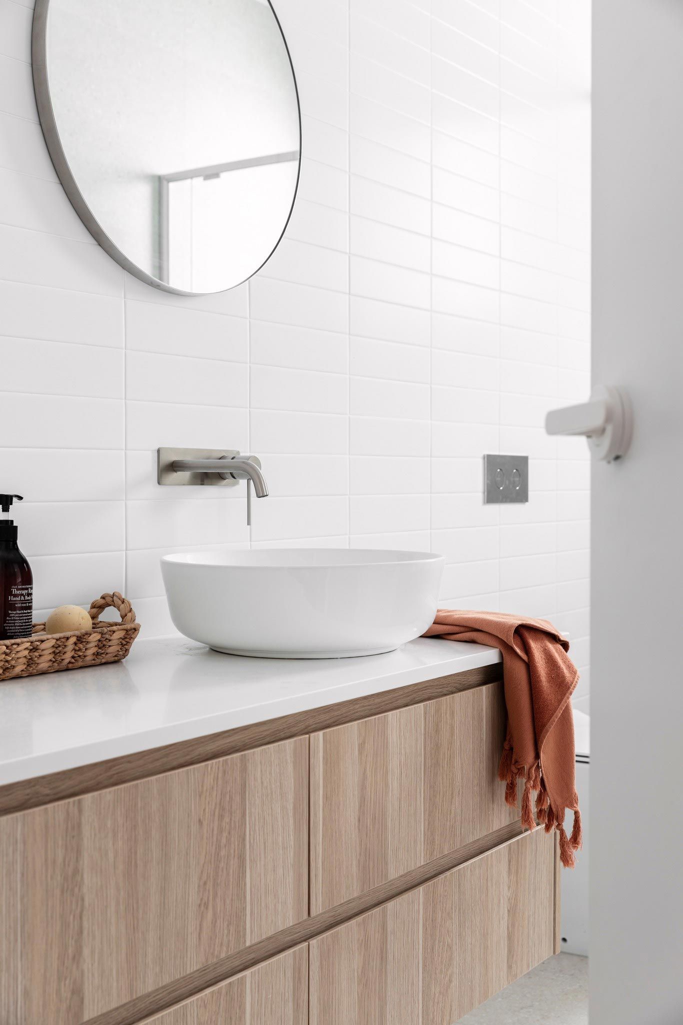 Modern bathroom with white vessel sink, wooden vanity, and orange towel.