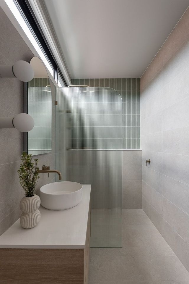 Modern bathroom with a white sink, shower with textured green tiles, and neutral tones.
