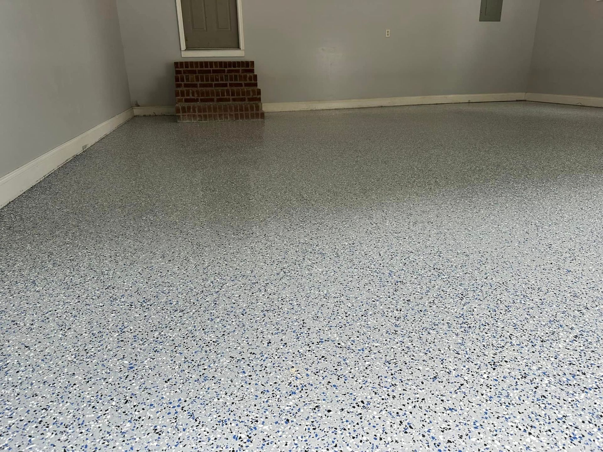 Empty speckled floor in a small room with white walls and a window vent on the far wall