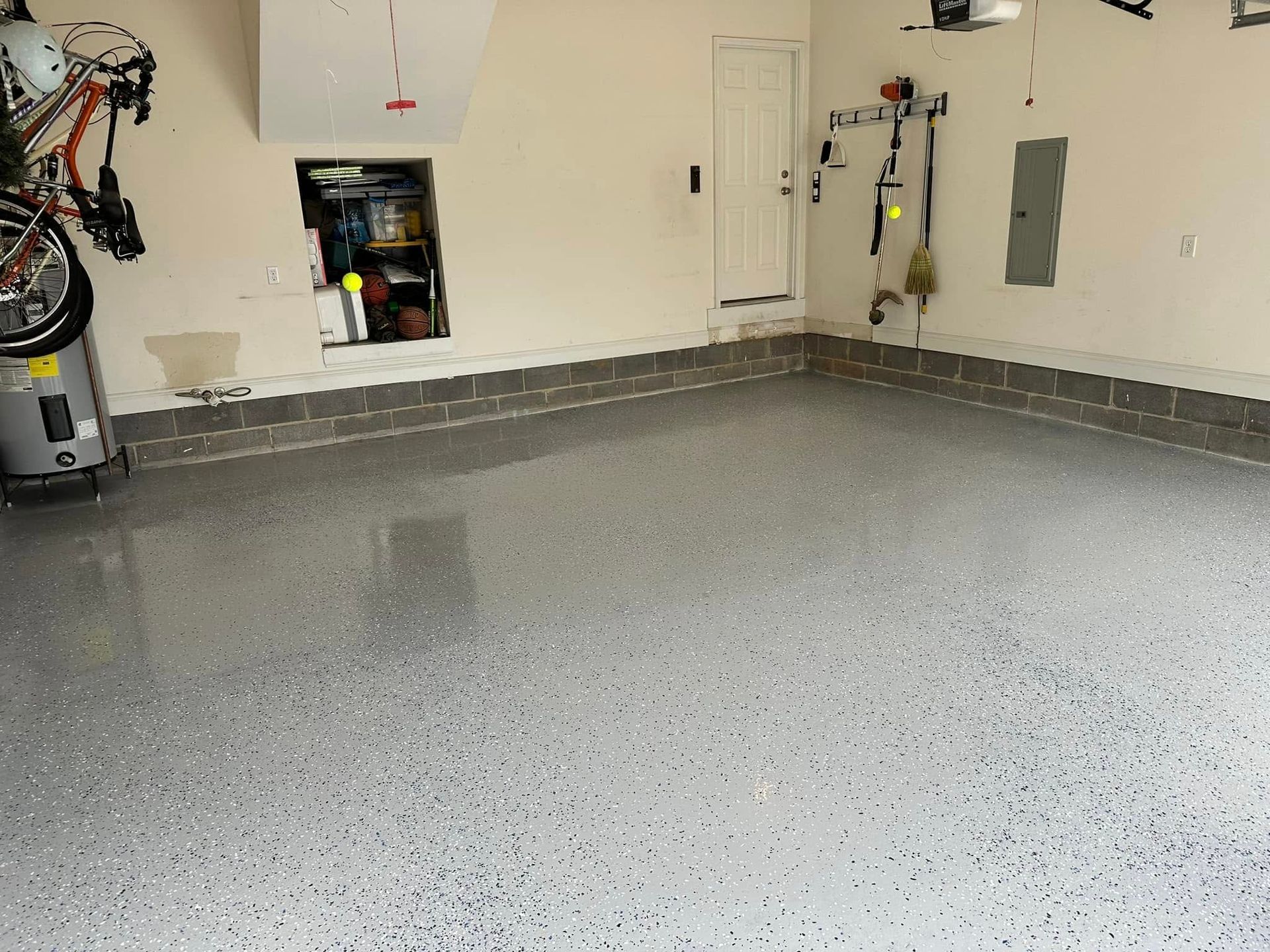 Empty garage with a speckled gray floor, white walls, and a wall-mounted utility box and tools.