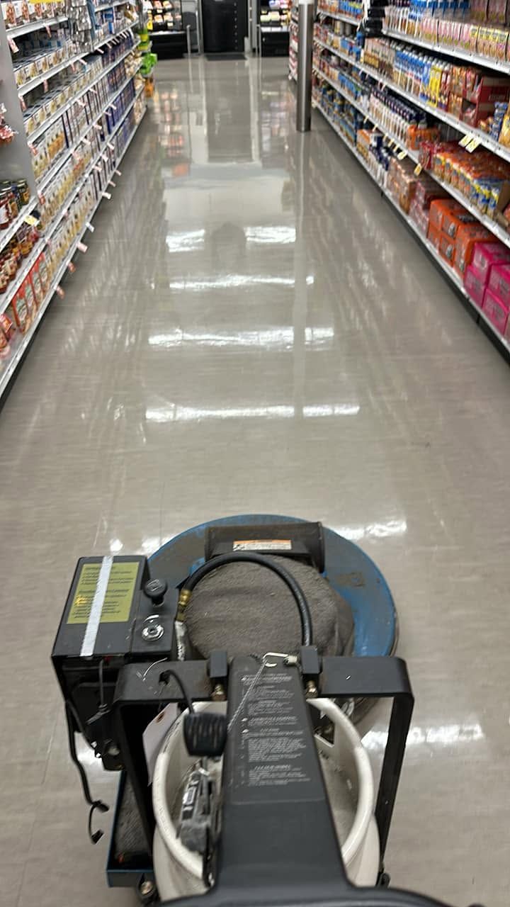 A floor-cleaning machine in a grocery store aisle with shelves on both sides.