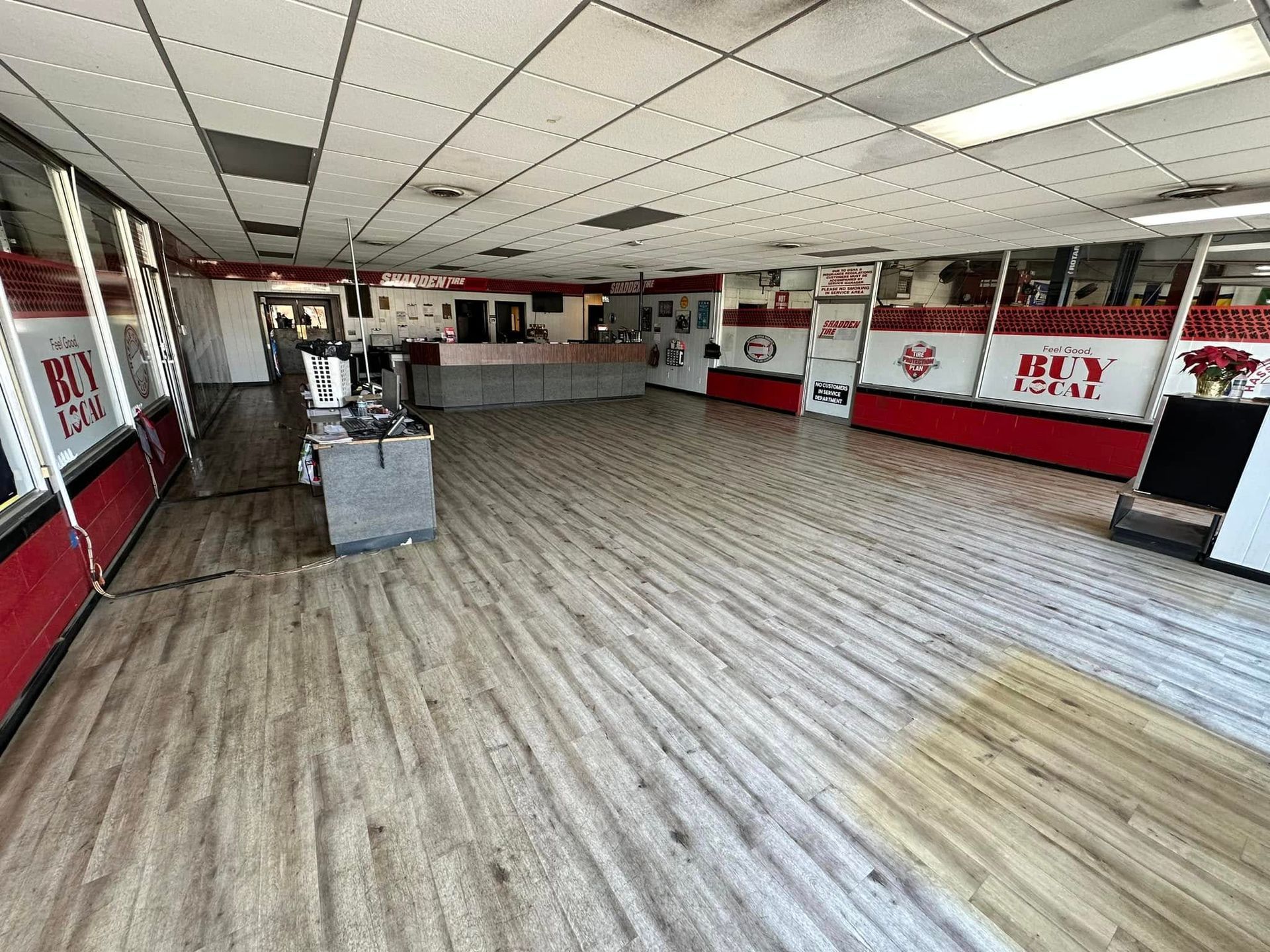Empty retail storefront with wood-look floor, white ceiling tiles, and red-and-white wall panels
