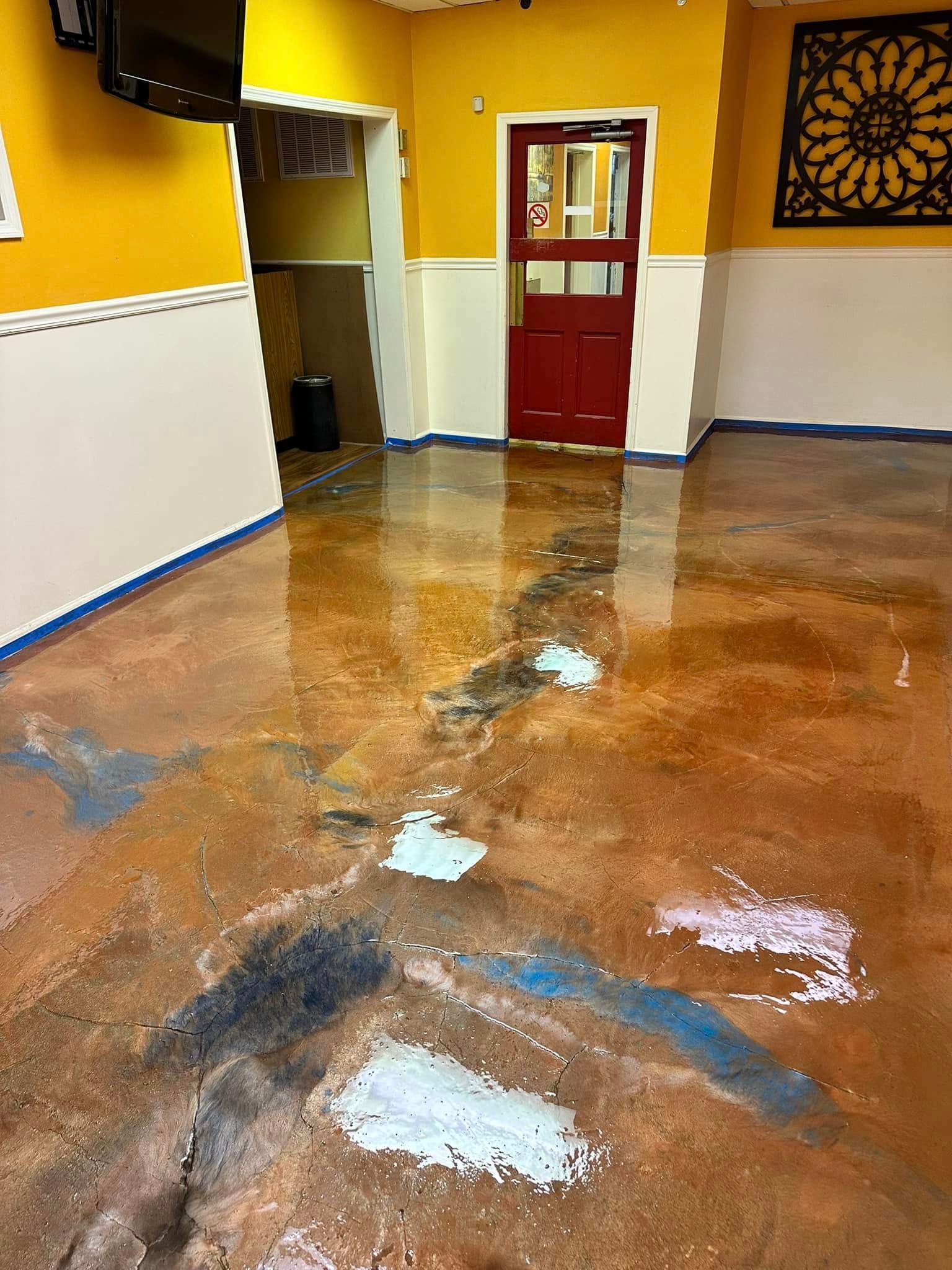Wet hallway floor reflecting light, with yellow walls, a red door, and a doorway in the back.