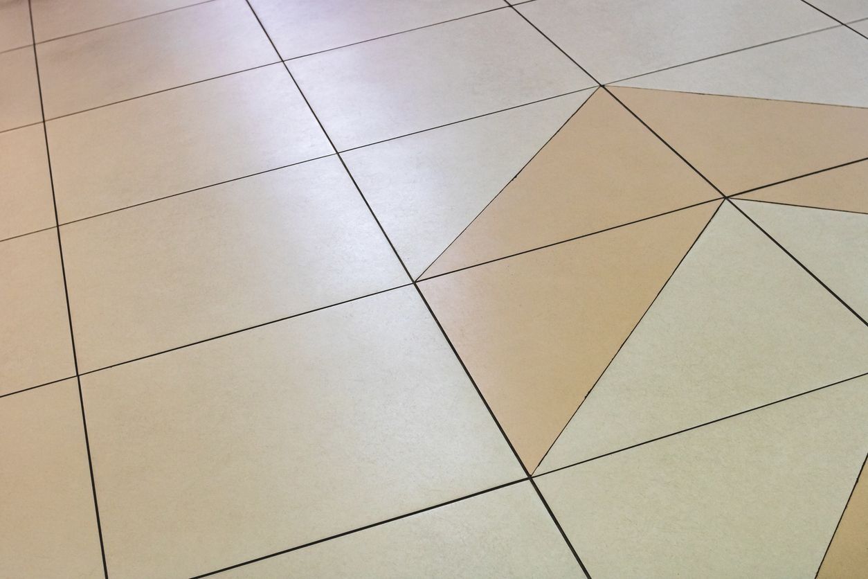 Close-up of beige tiled floor with dark grout lines and a geometric tan-and-white inlay.