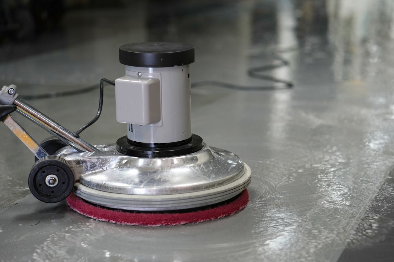 Floor cleaning machine scrubbing a shiny concrete floor in an indoor facility