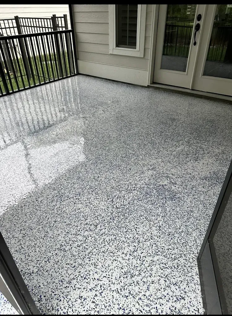 Speckled gray patio floor beside sliding doors and black railing on a covered porch