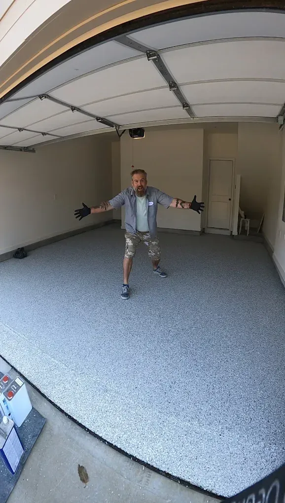 Man standing in an empty garage with arms outstretched, near the open door.