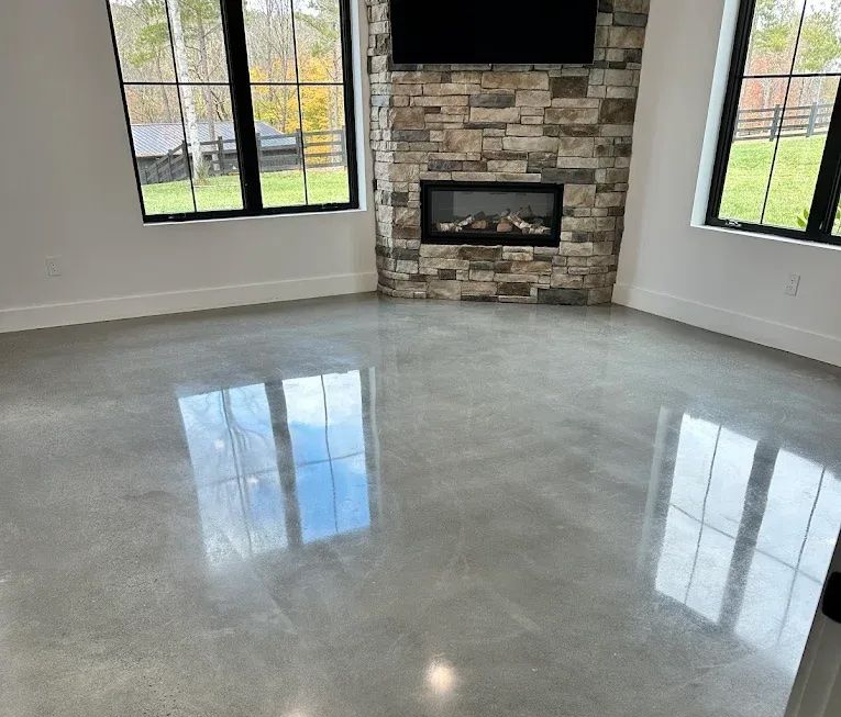 Empty modern living room with polished concrete floor, stone fireplace, and large windows reflecting light
