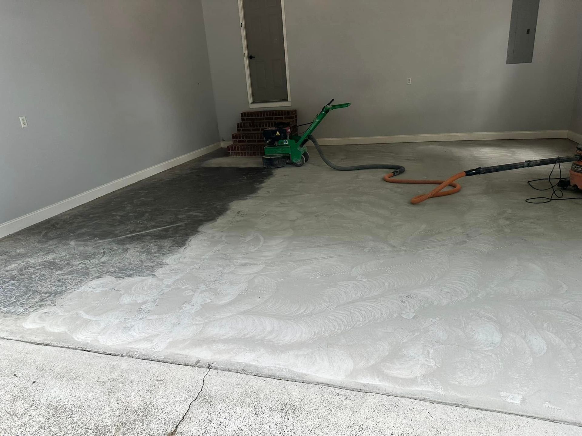Partially finished concrete floor in a garage, with tools and an extension cord near the wall.