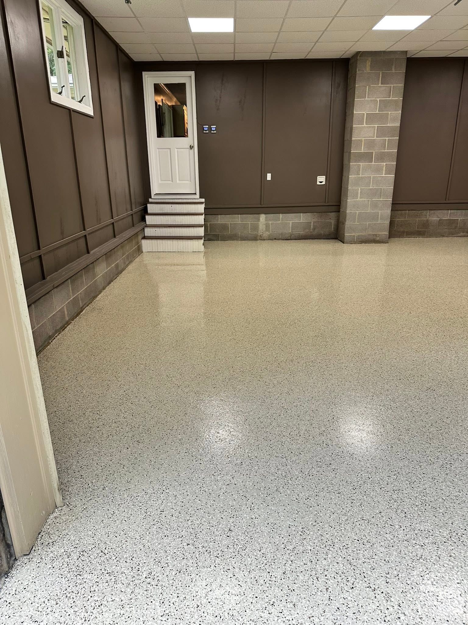 Empty indoor room with speckled floor, brown walls, and a white doorway at the back