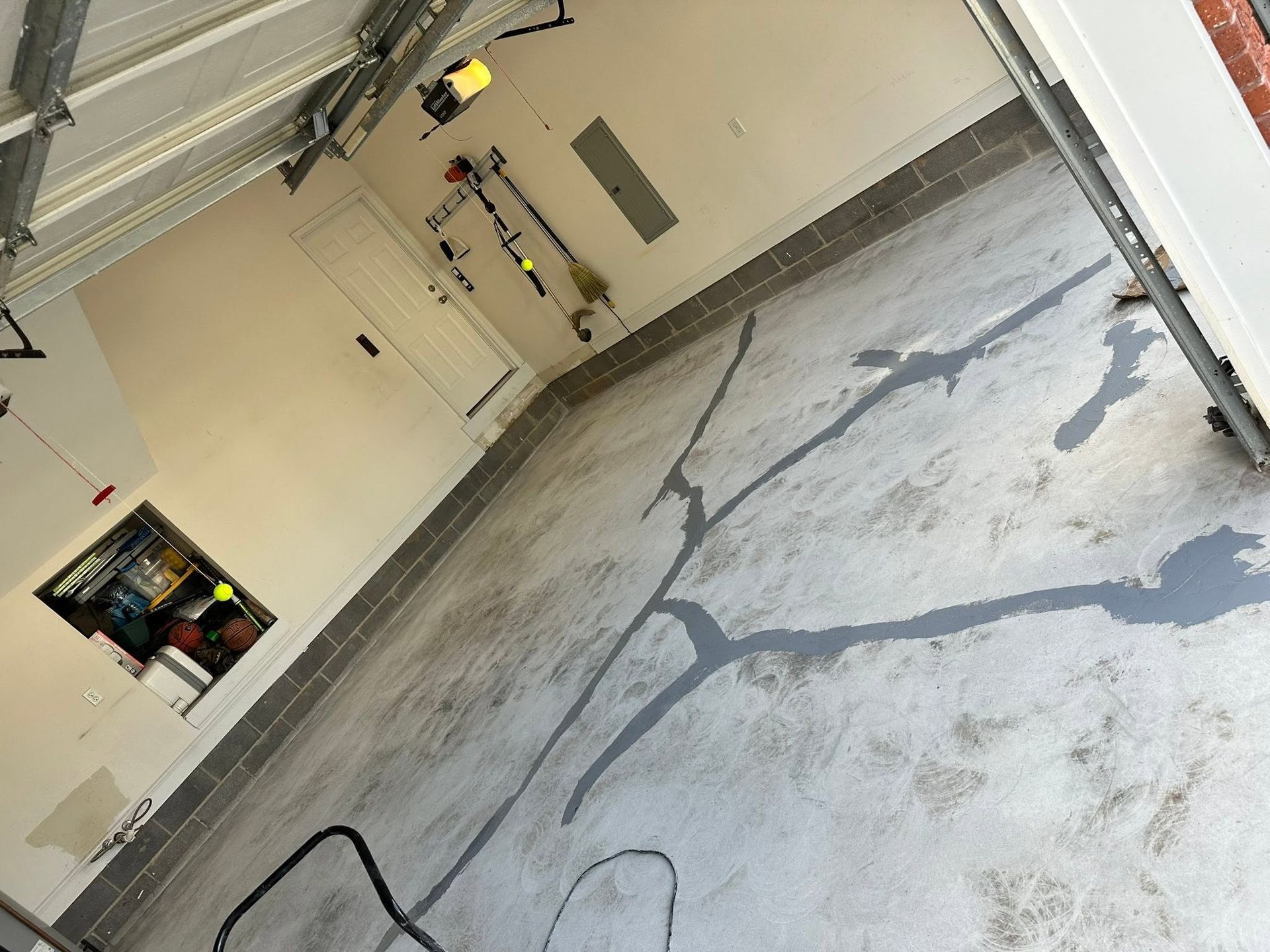 Empty garage with cracked concrete floor, wall shelves, and a utility panel.