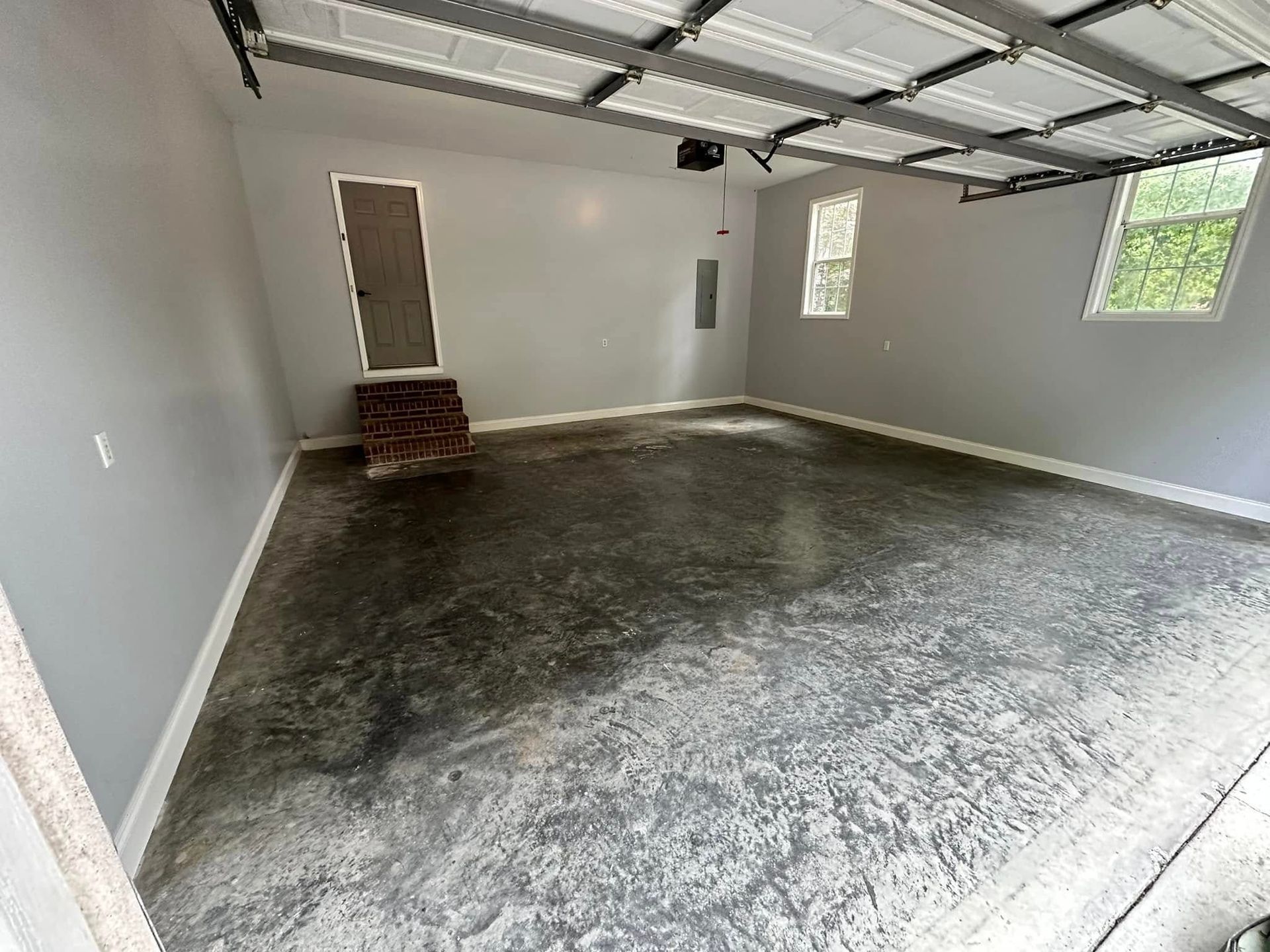 Empty garage interior with unfinished concrete floor, white walls, and open overhead door tracks.