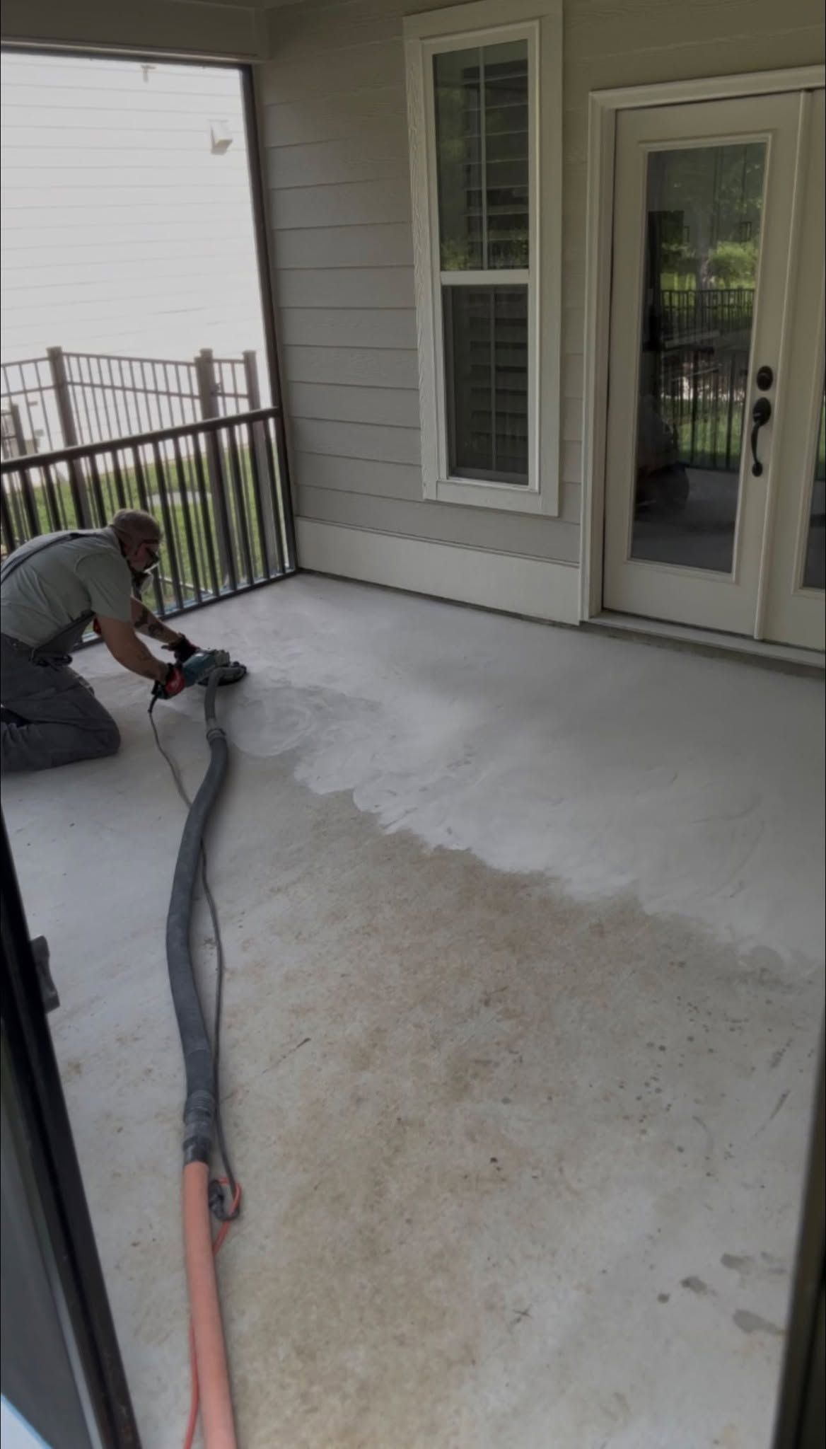 Worker power-washing a concrete porch near a sliding glass door and railing