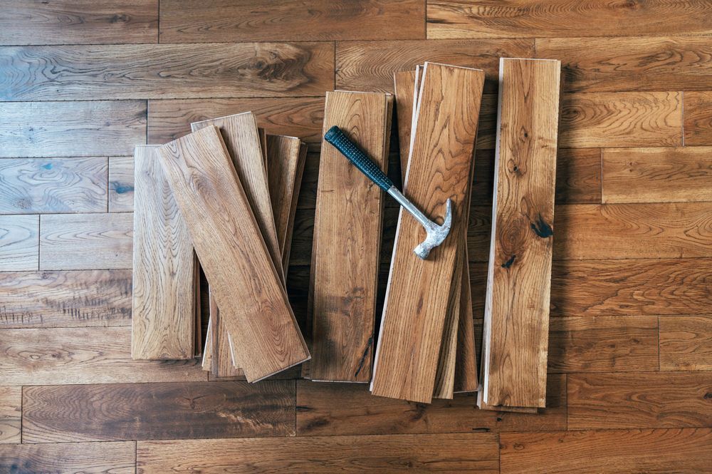 A hammer is sitting on top of a pile of wooden planks on a wooden floor.