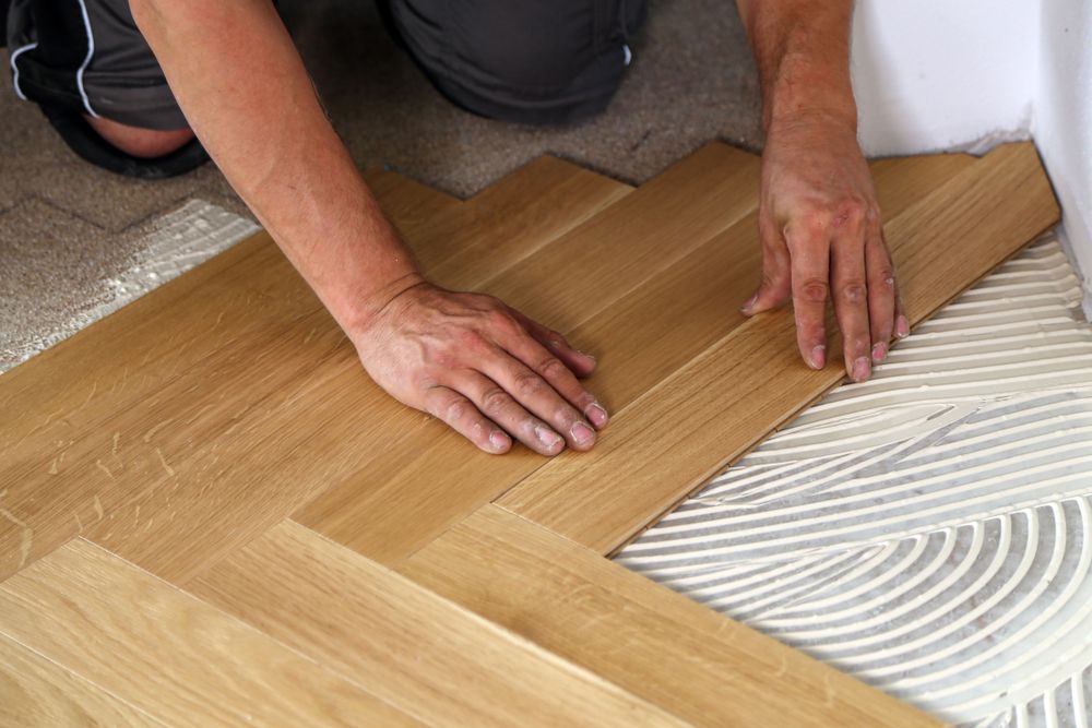A man is installing a wooden floor with glue.
