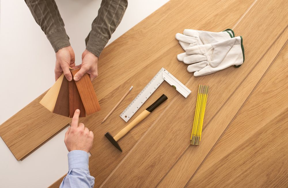 A person is holding a piece of wood next to a hammer and ruler.
